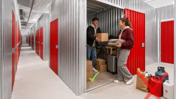 Doi tineri depozitează cutii și textile într-un spațiu City Storage Cluj, lângă exemple de obiecte interzise.